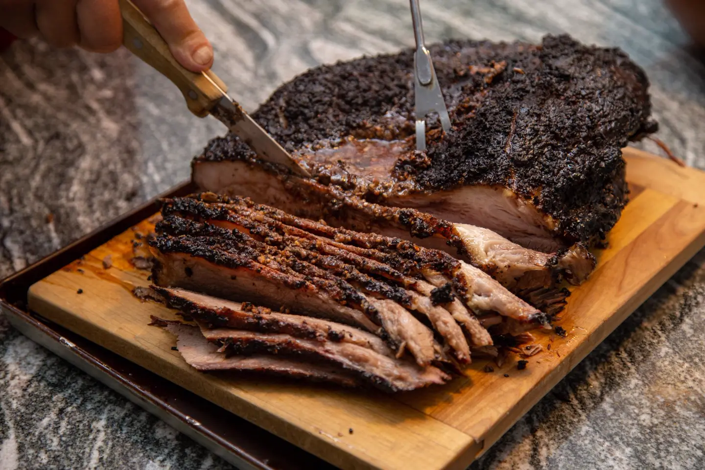 Smoked brisket with a dark bark being sliced on a wooden cutting board